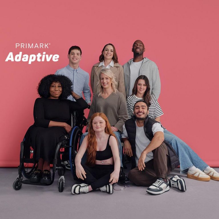 8 adults are posing together in various Primark branded clothing. They have various disabilities- one person being a wheelchair user, another showing off her feeding tube in a cropped top. There is a pink background behind them, with the text “Primark: Adaptive”.